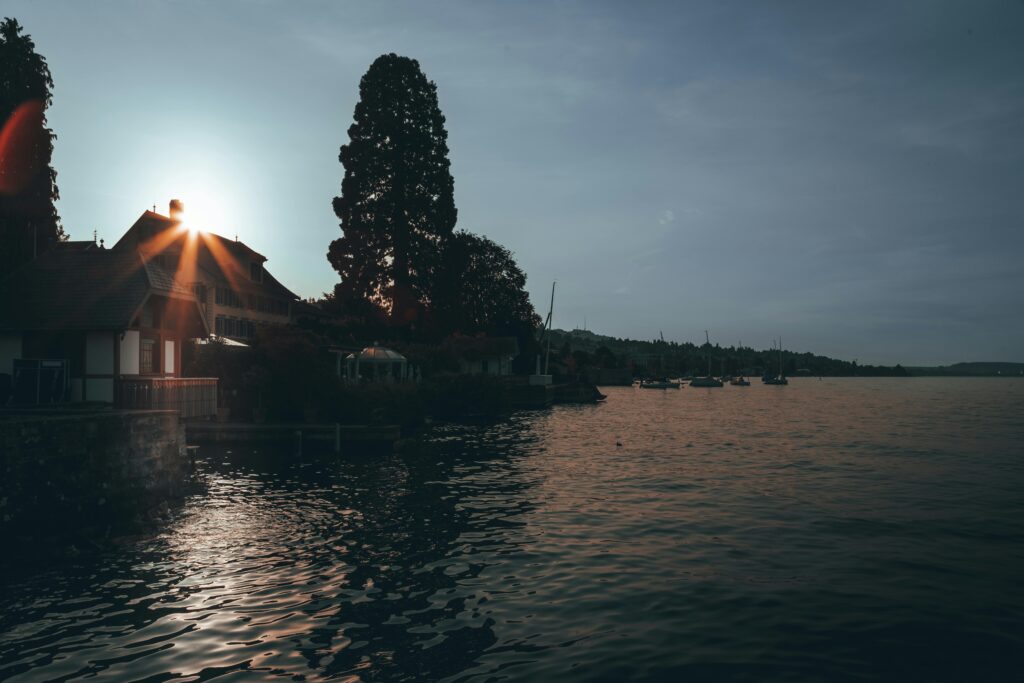 Serene sunset over Lake Zurich capturing silhouette of a house with boats and distant trees.